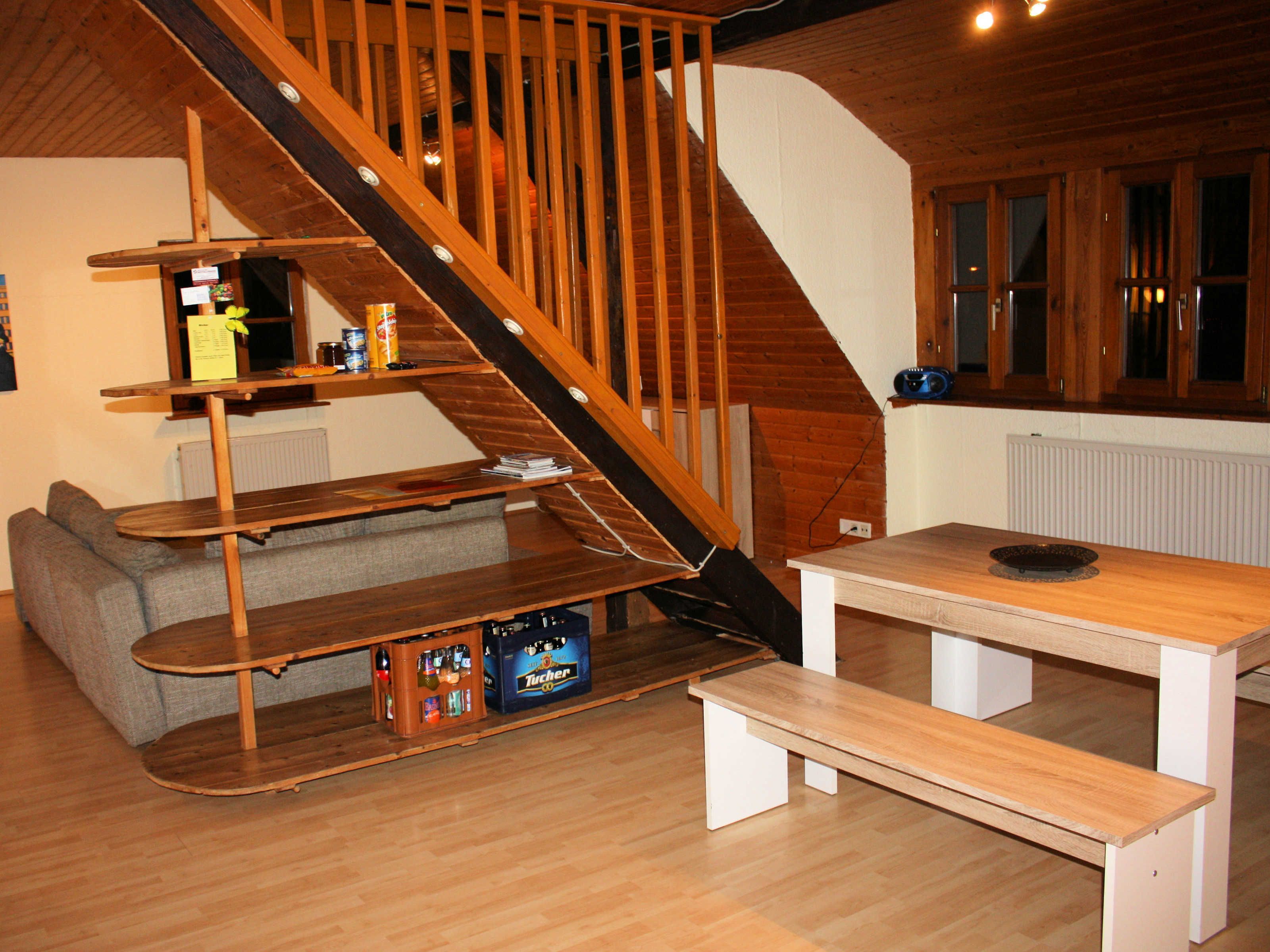 A wooden staircase leading to a loft bedroom with a bed, a wooden table, and a bench.
