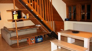 Una escalera de madera que lleva a un dormitorio en un altillo con una cama, una mesa de madera y un banco.