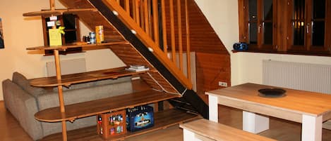 A wooden staircase leading to a loft bedroom with a bed, a wooden table, and a bench.