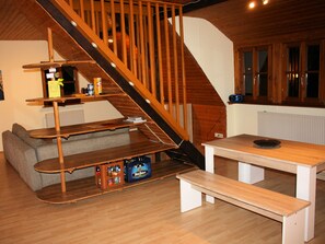 Una escalera de madera que lleva a un dormitorio en un altillo con una cama, una mesa de madera y un banco.