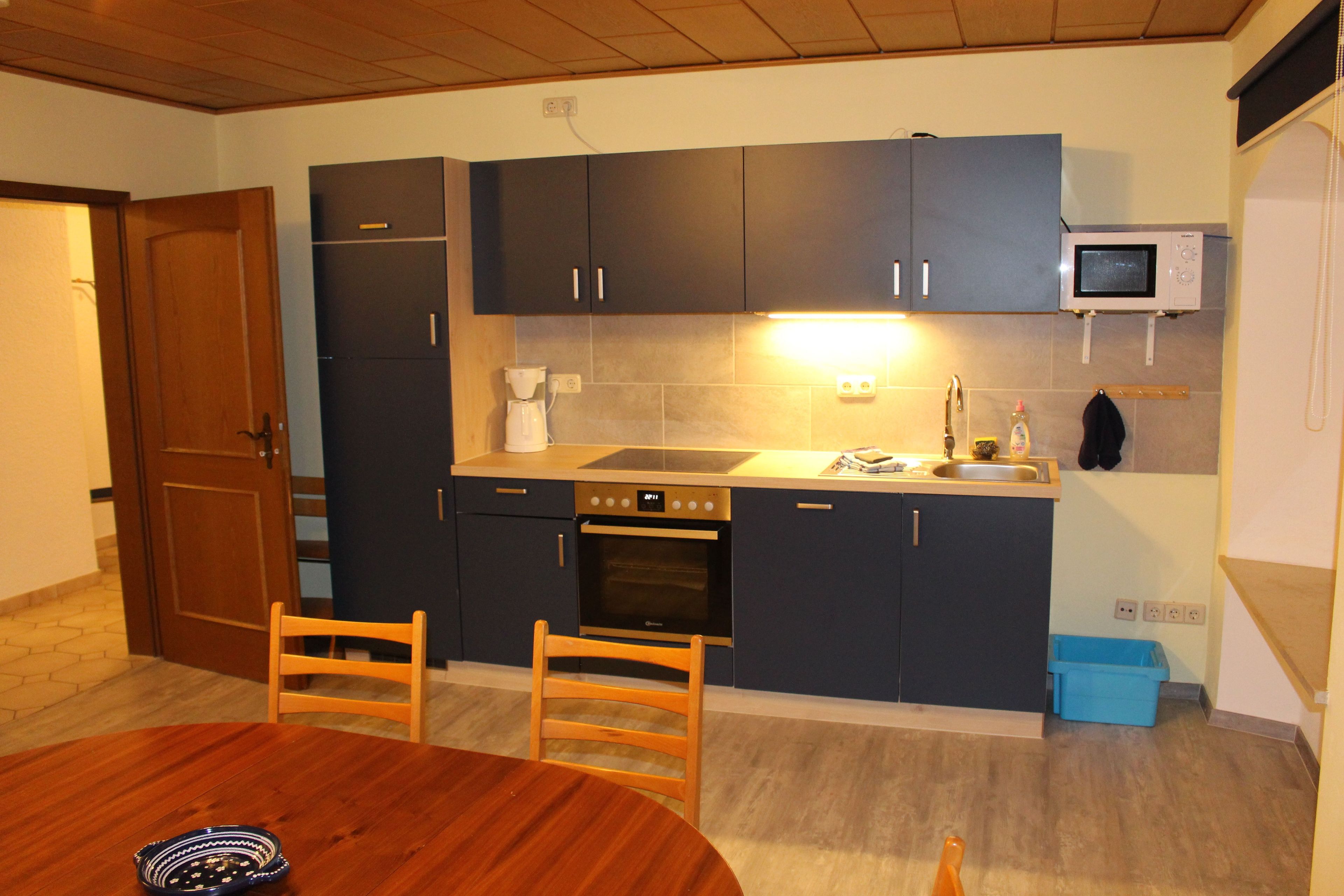 A compact kitchen with dark cabinets, a microwave, an oven, a sink, and a dining table with chairs.