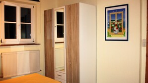 Un dormitorio con una cama de madera, un armario, un radiador, una ventana y un cuadro enmarcado en la pared.