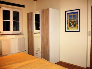 Un dormitorio con una cama de madera, un armario, un radiador, una ventana y un cuadro enmarcado en la pared.
