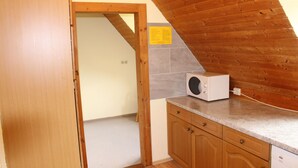 A kitchen with wooden cabinets, a microwave, and a tiled backsplash. - Category C: 3-room apartment for 4 persons - Pension Mühle (Egloffstein)