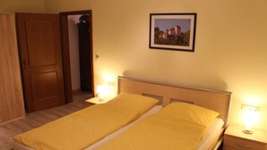 A double bed with two bedside tables, each with a lamp, a framed picture on the wall, and a wooden wardrobe. - Category C: 3-room apartment for 4 persons - Pension Mühle (Egloffstein)