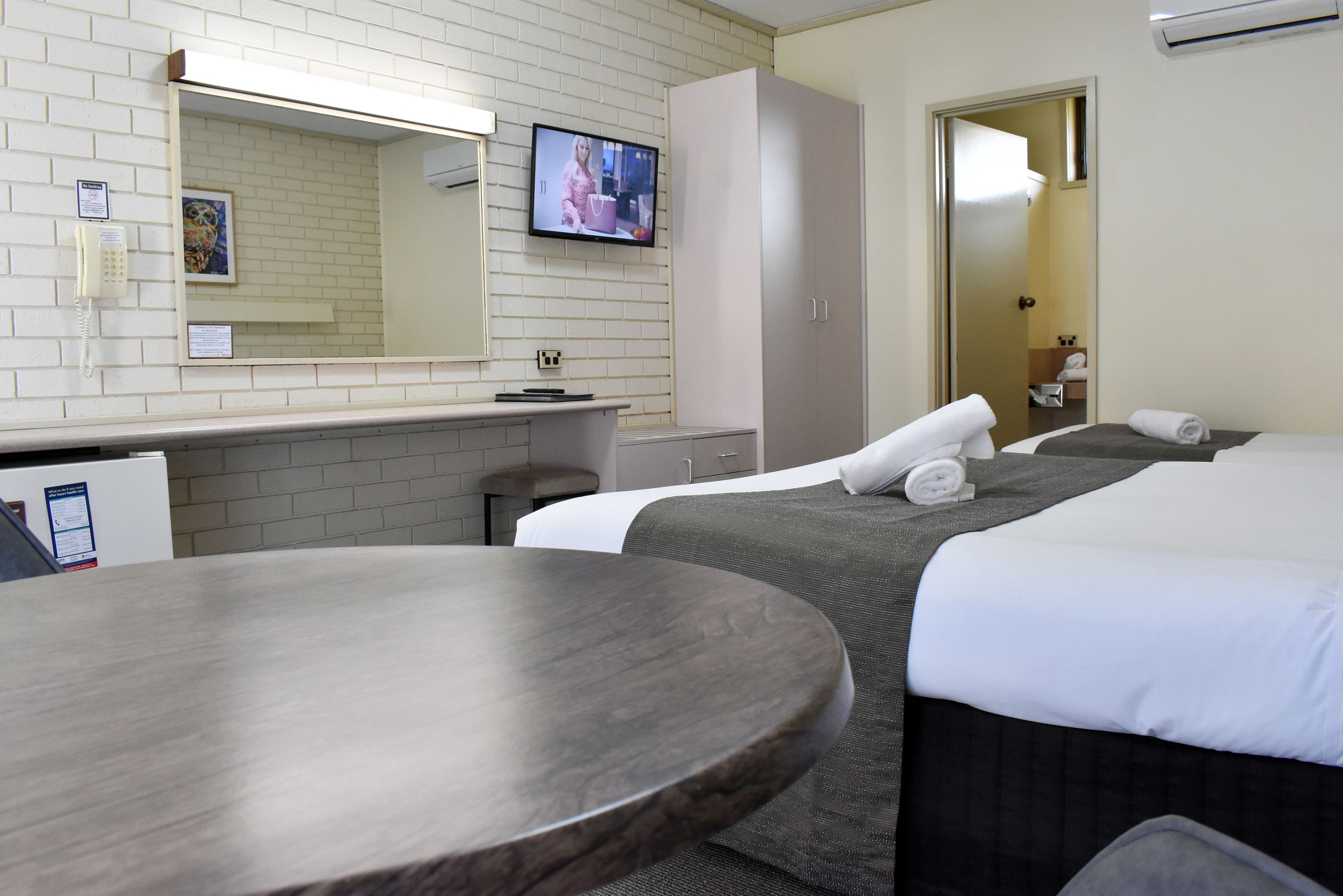 A hotel room with two beds, a desk, a chair, a round table, a TV, and a wardrobe.