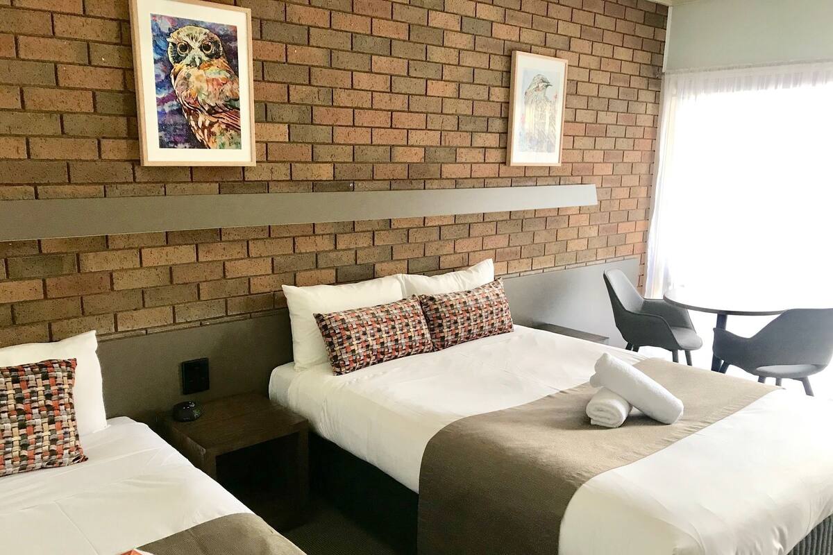 Una camera d'albergo con due letti, un muro in mattoni e una finestra che dà sul panorama esterno.