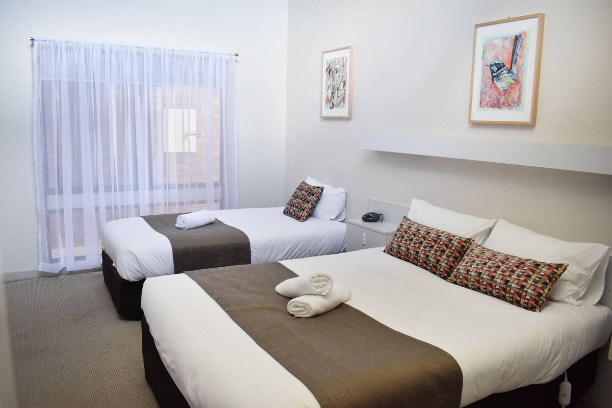 Una camera d'albergo con due letti, una finestra con tende leggere e opere d'arte alle pareti.