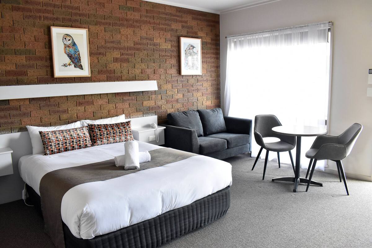 Camera d'albergo con un letto grande, un divano, un tavolino con sedie e due quadri appesi al muro in mattoni.