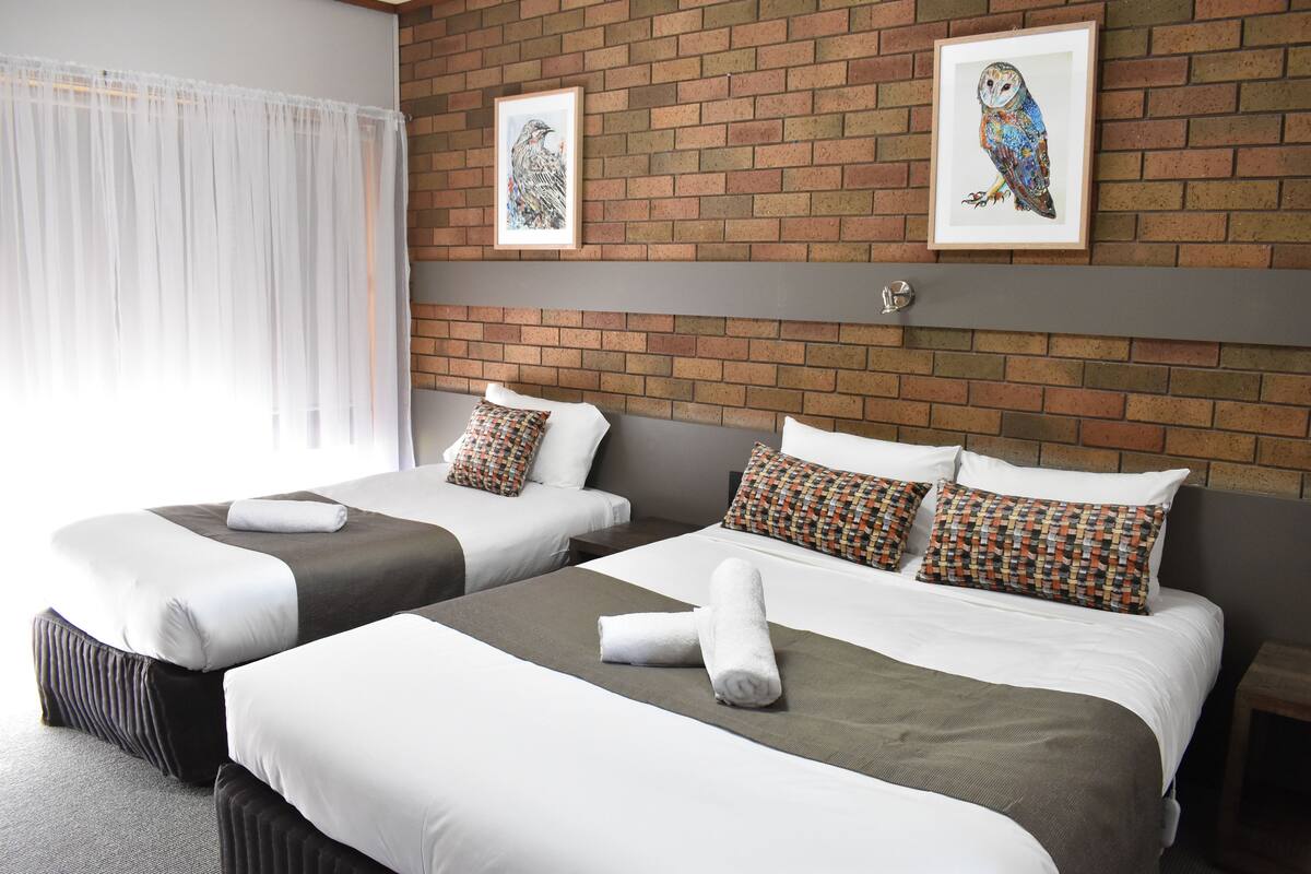 Camera d'albergo con due letti, un muro in mattoni e due opere d'arte incorniciate.