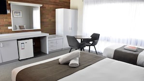 Quarto de hotel com cama, escrivaninha, cadeira, guarda-roupa e um pequeno frigorífico.