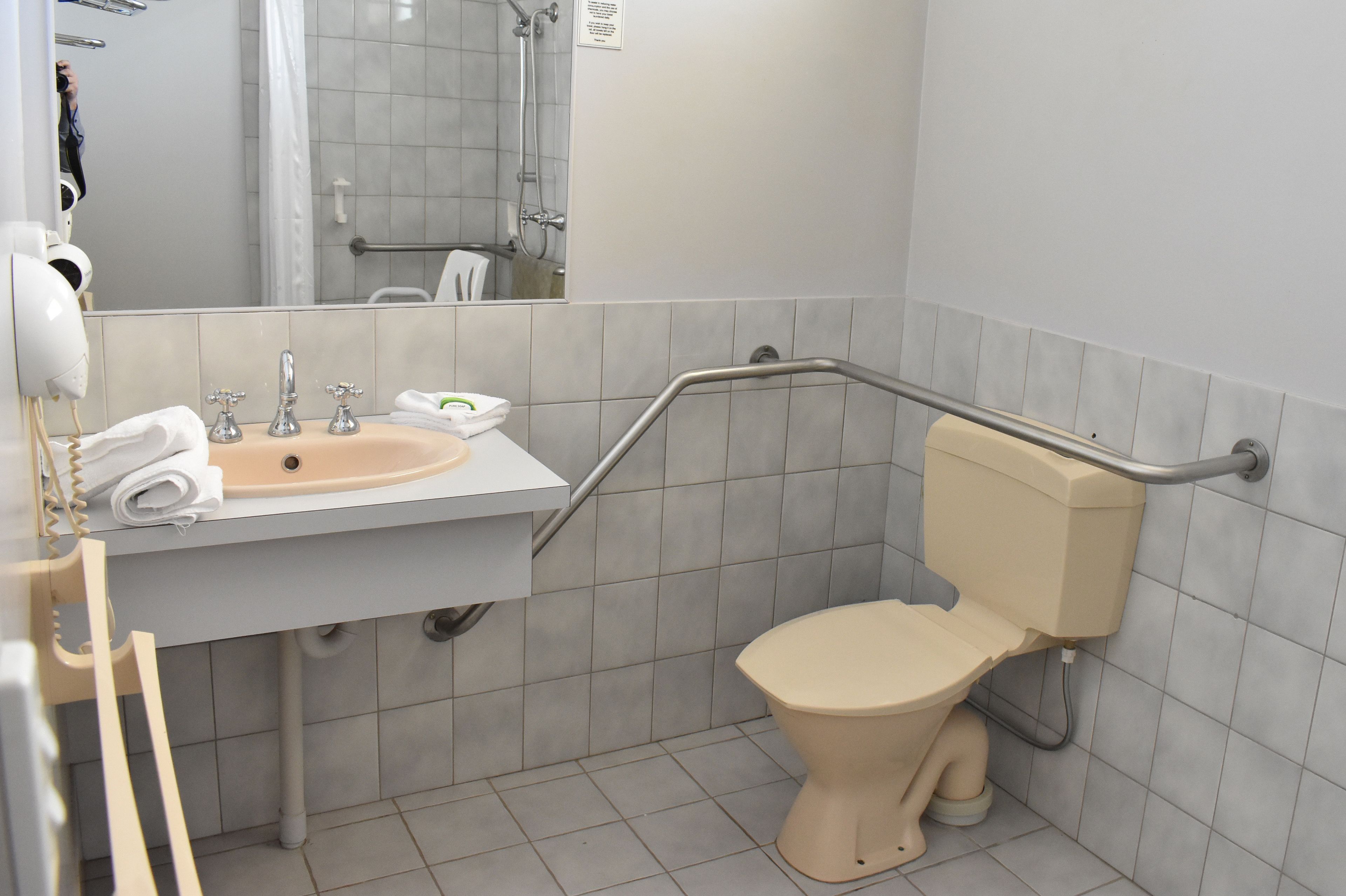 A bathroom with a sink, mirror, toilet, and grab bars.