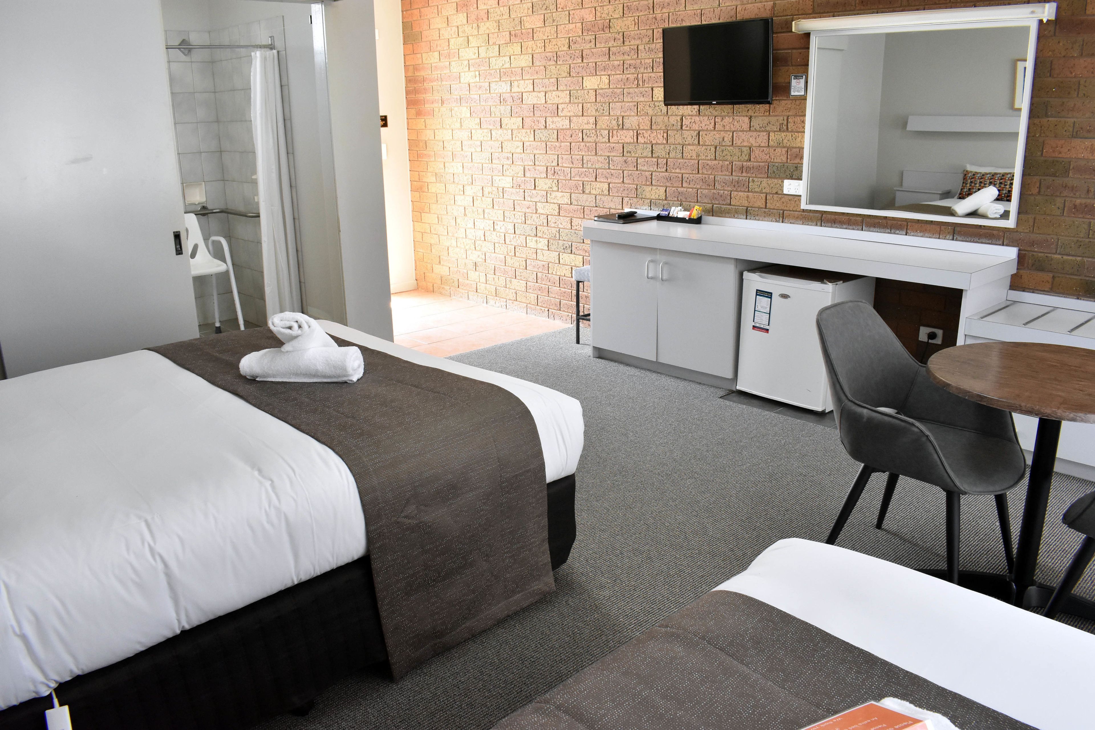 A hotel room with a bed, a desk, a chair, a shower, and a TV mounted on the wall.