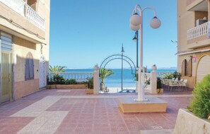A courtyard with a view of the sea, a gate, outdoor seating, and a lamp post.