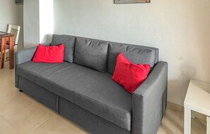 Een grijze bank met twee rode kussens in een kamer met een witte muur en een witte tafel.
