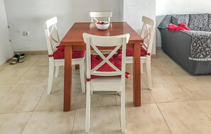 Een eettafel met vier witte stoelen, elk met een rode kussen. Er staat een schaal met fruit op de tafel.