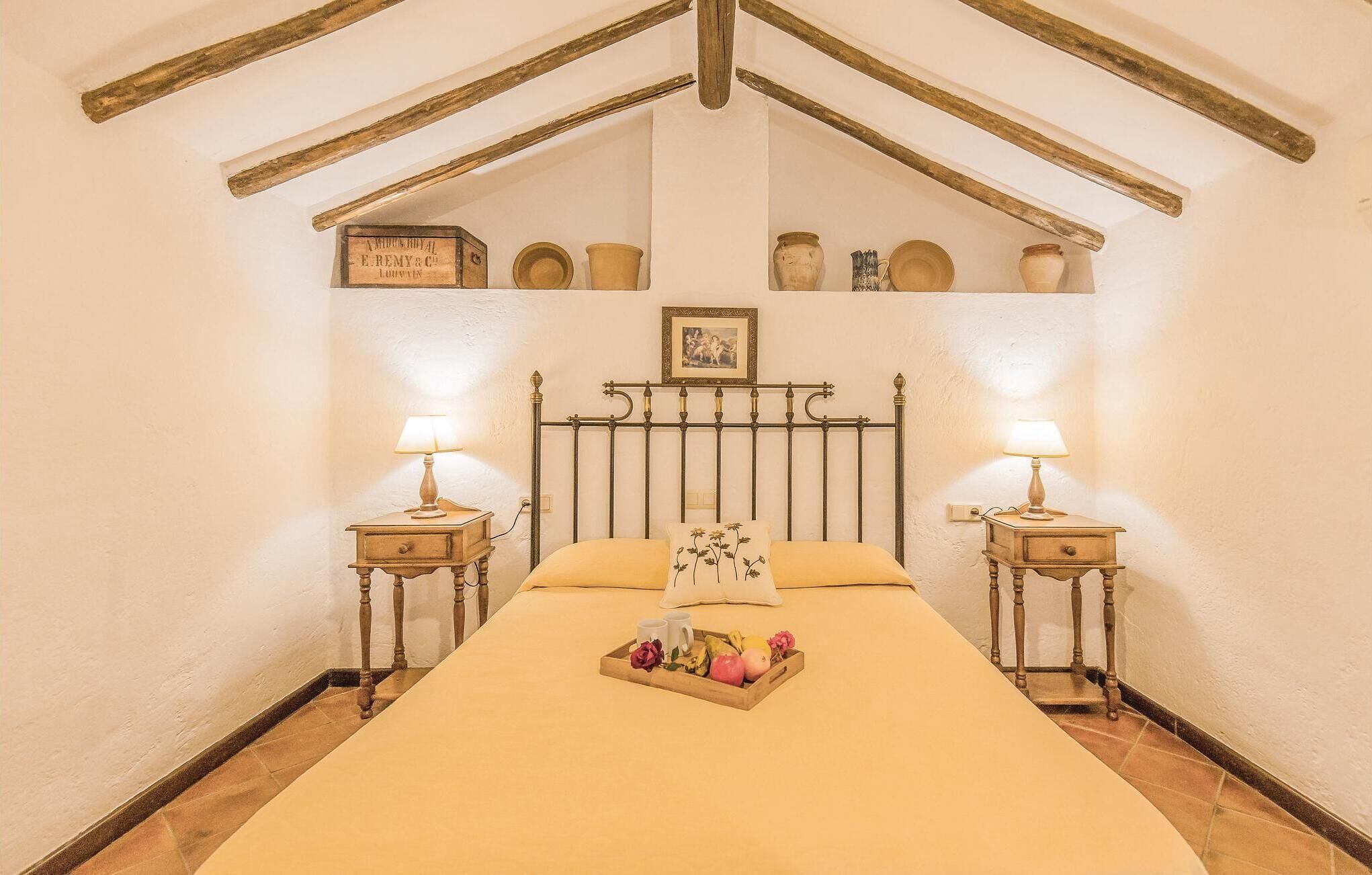 Ein Schlafzimmer mit einem Bett, zwei Nachttischen mit Lampen, einer Fruchtschale und einem Regal mit Dekoration.