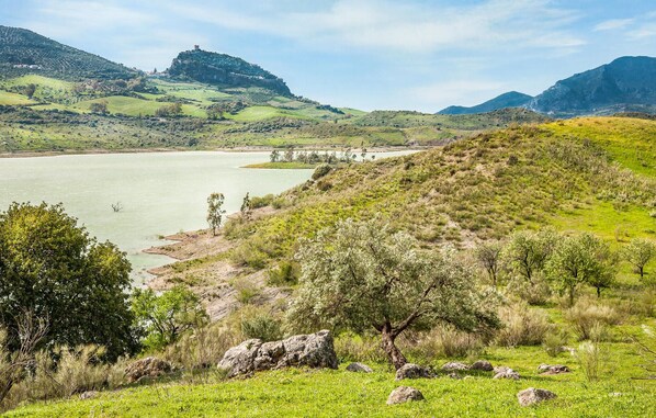 Un paisaje pintoresco con una colina, una masa de agua y una estructura distante que se asemeja a un castillo.