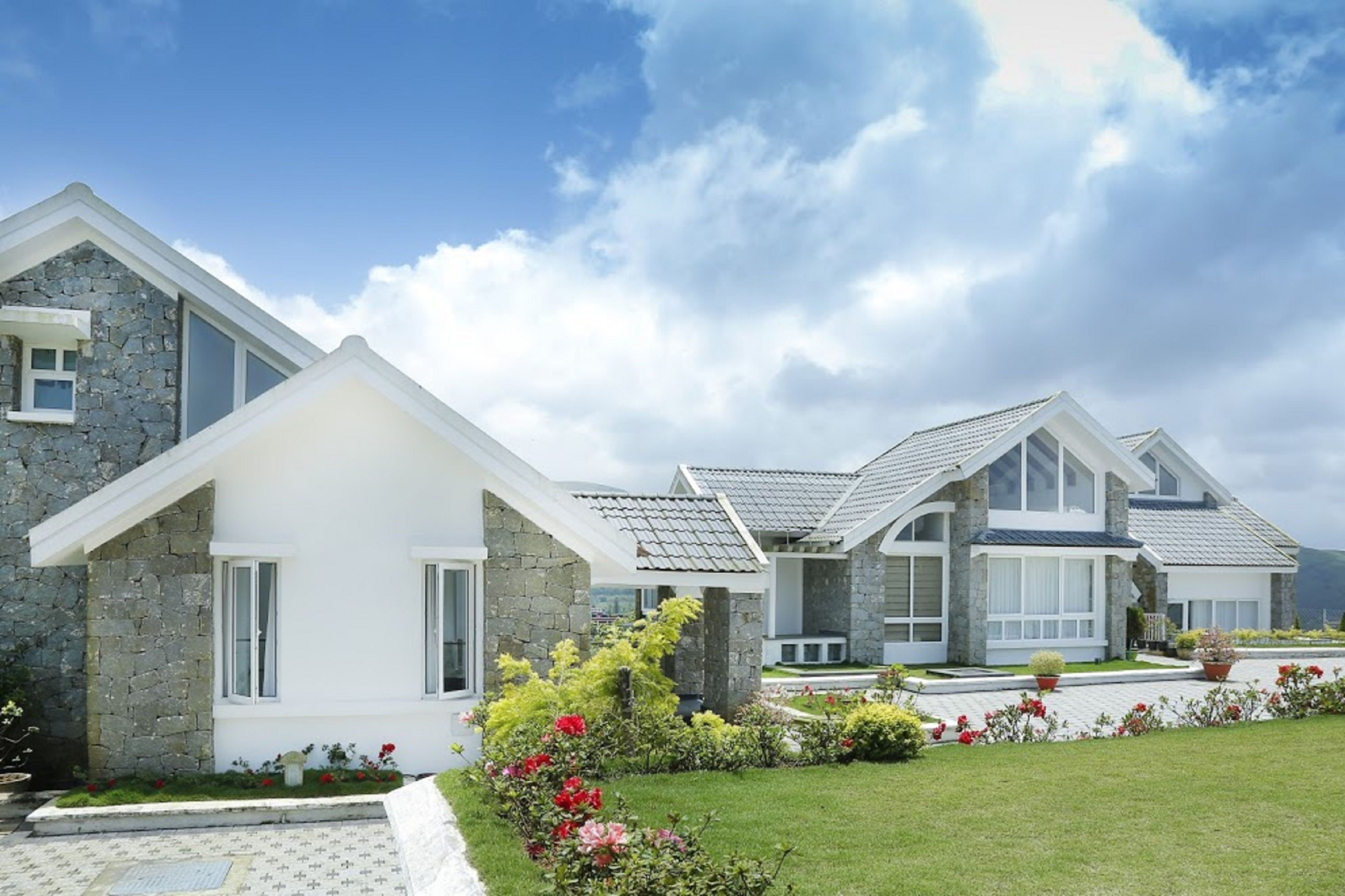 A modern house with stone and white exterior walls, large windows, and a well-maintained garden with red flowers.