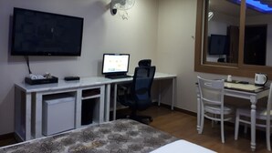 A hotel room with a bed, a desk with a computer, a chair, a TV, and a ceiling fan. - Breakfast at Tiffany's Motel (Mokpo)