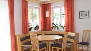 Un comedor con una mesa redonda y seis sillas, un banco empotrado y ventanas grandes con cortinas.