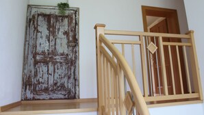 Una escalera de madera con barandilla, una puerta rústica con pintura descascarada y una planta pequeña en la parte superior.