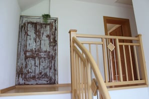 Un escalier en bois avec une rampe, une porte rustique dont la peinture s’écaille et une petite plante posée sur le dessus.