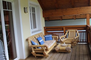 Una terraza de madera con sofá, sillas, una ventana y barandilla.