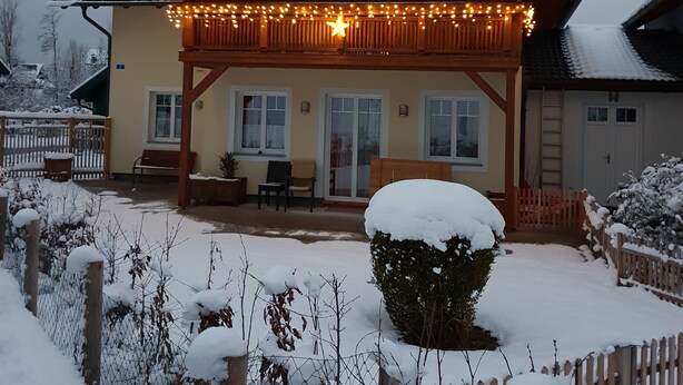Una cabaña de dos pisos con balcón, barandillas de madera y techo cubierto de nieve.