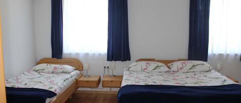 Una habitación con dos camas individuales, cabeceros de madera, mesitas de noche con lámparas y una ventana con cortinas.