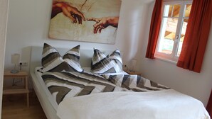 Un dormitorio con cama, almohadas, una mesita de noche, una lámpara y un cuadro en la pared.