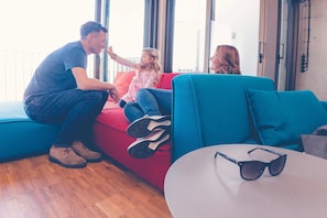 Un salon moderne avec un canapé rouge, un divan bleu et une table ronde sur laquelle sont posées des lunettes de soleil.