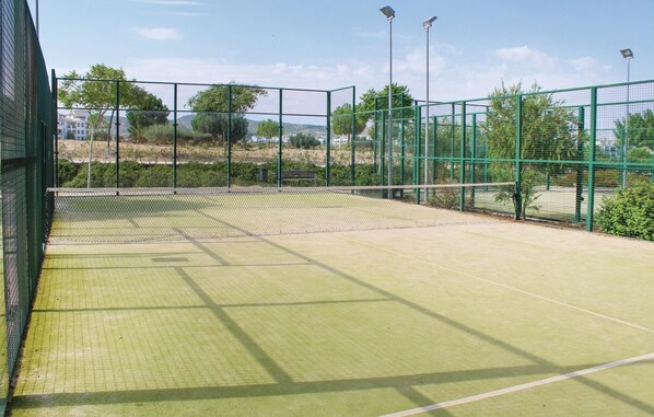 Un court de tennis en plein air, entouré d’une clôture verte, éclairé par des lampes solaires, et avec un ciel dégagé.