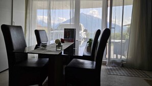 Un comedor con una mesa y sillas, un jarrón con flores y vistas a montañas a través de cortinas traslúcidas.