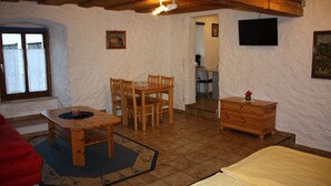 Een kamer met een houten tafel en stoelen, een bed, een kast, een televisie en een raam.