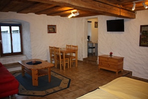 Een kamer met een houten tafel en stoelen, een bed, een kast, een televisie en een raam.