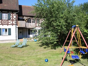 A residential property with a two-story house, a swing set, and two striped lawn chairs. - Category A: 1-room apartment for 2 persons - Pension Mühle (Egloffstein)