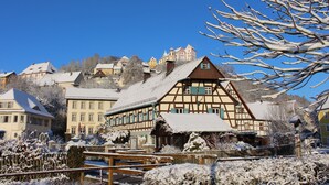 Ein traditionelles Fachwerkhäuschen mit schneebedecktem Dach, umgeben von anderen Gebäuden und blauem Himmel.