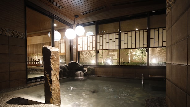 A traditional Japanese onsen with a stone bath, wooden walls, and a view of the outdoors through a shoji screen. - Dormy Inn Premium Osaka Kitahama Hot Springs (Osaka)