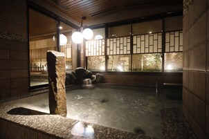 A traditional Japanese onsen with a stone bath, wooden walls, and a view of the outdoors through a shoji screen.