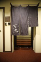 A hotel entrance with a wooden bench and a sign with Japanese characters.