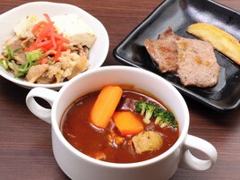 A meal consisting of a soup with vegetables, a bowl of rice with vegetables, and a plate with meat and a fried item.