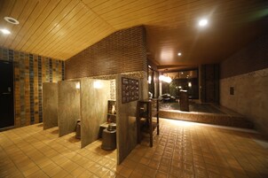 A public restroom with tiled floors, wooden ceiling, and a brick accent wall.