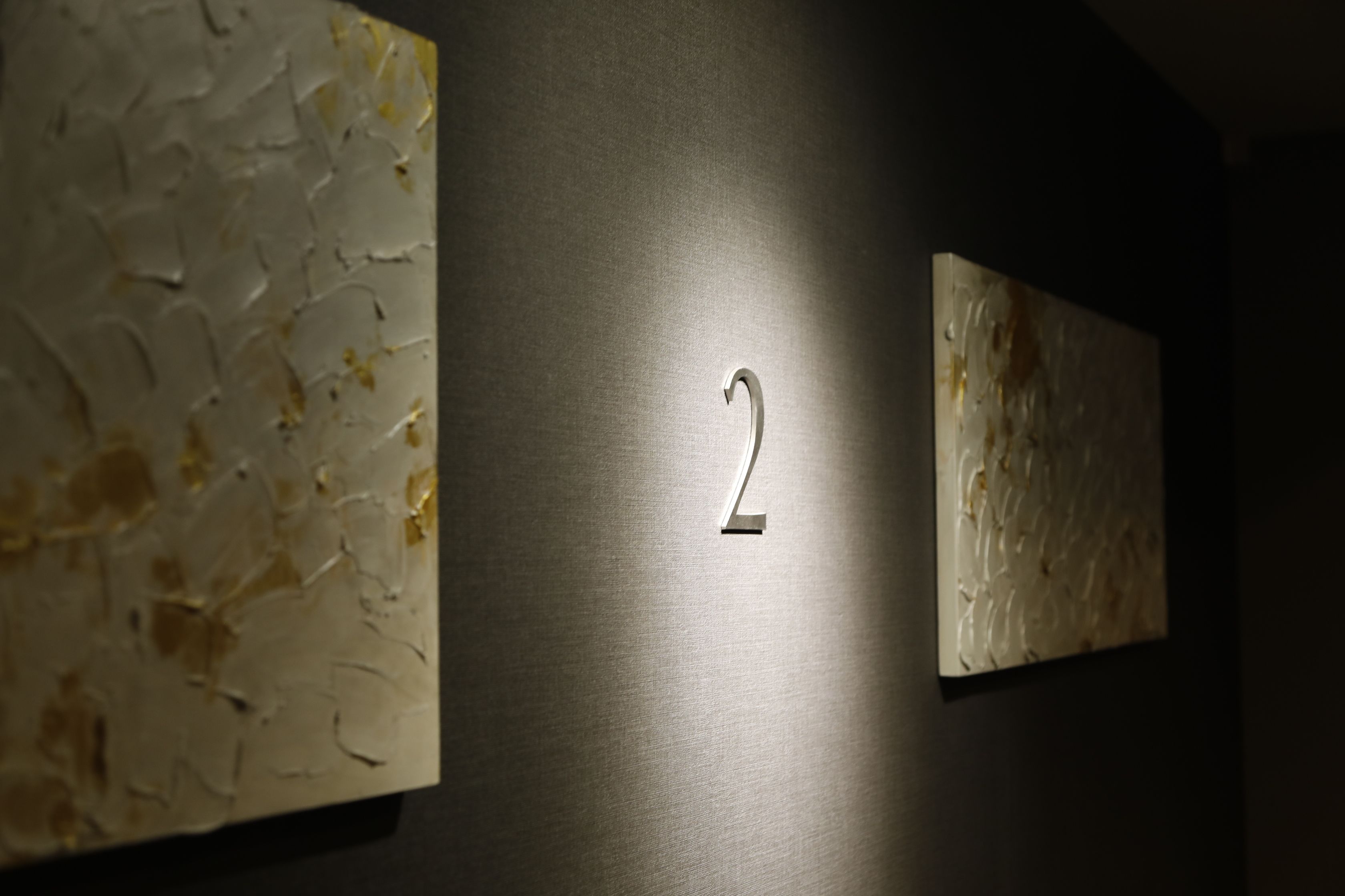 A wall with two textured paintings and a number '2' illuminated in the center.