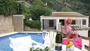 Une table dressée pour deux, une bouteille de vin et un vase de fleurs, le tout installé au bord de la piscine.