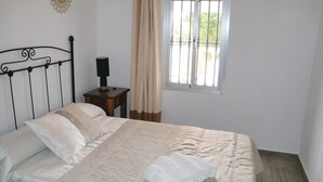 Un lit bien fait, avec une couvre-lit à motifs et des oreillers, une table de chevet avec une lampe, et une fenêtre avec des rideaux.