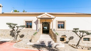 A building with a stone facade, a central entrance with steps, and two windows with metal bars.