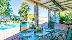 A glass table set for dining outdoors with a pool and lounge chairs in the background.