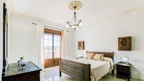 A bedroom with a wooden bed, a nightstand, a dresser, a chandelier, and a window with curtains.