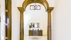 A hallway with a large wooden archway, a mirror above a wooden cabinet, and a chandelier.
